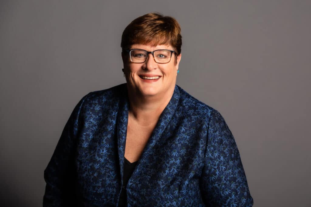 Diane in a blue jacket, grey background, smiling bio pic