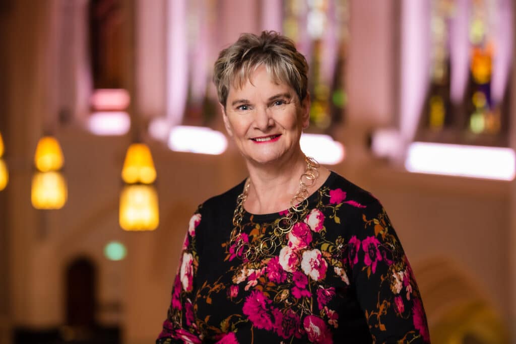Woman with short hair in floral shirt with stainglass backround